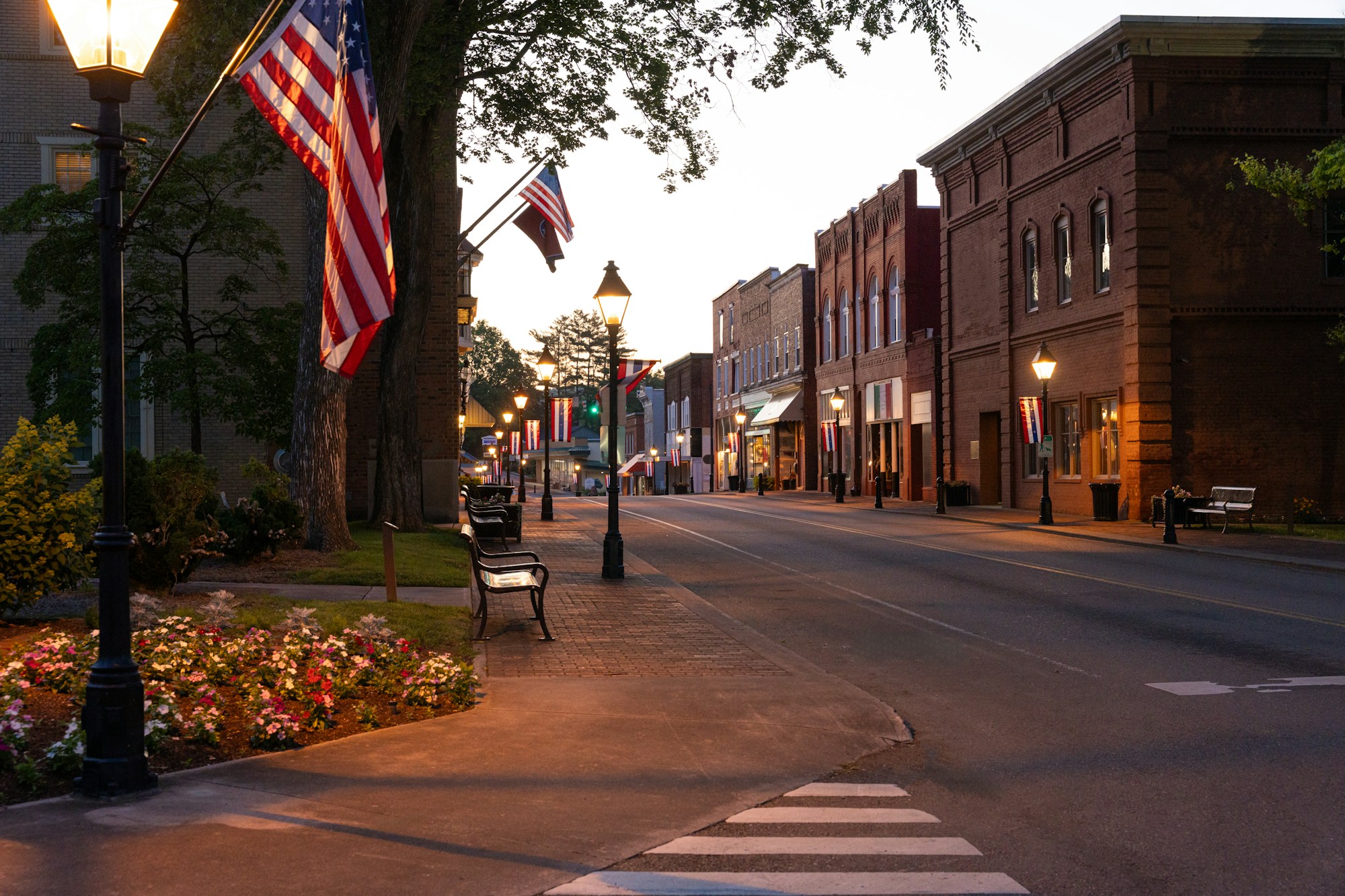 A small-town main street at dusk, with American flags on the lampposts